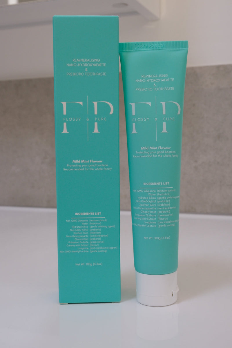 Flossy & Pure Mild Mint natural toothpaste, 100g tube beside its teal carton on a bathroom bench