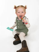 Smiling toddler brushing her teeth while holding a tube of Flossy & Pure fluoride-free family toothpaste