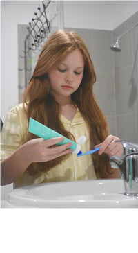 Girl squeezing Flossy & Pure nano-hydroxyapatite toothpaste onto her toothbrush at the bathroom sink