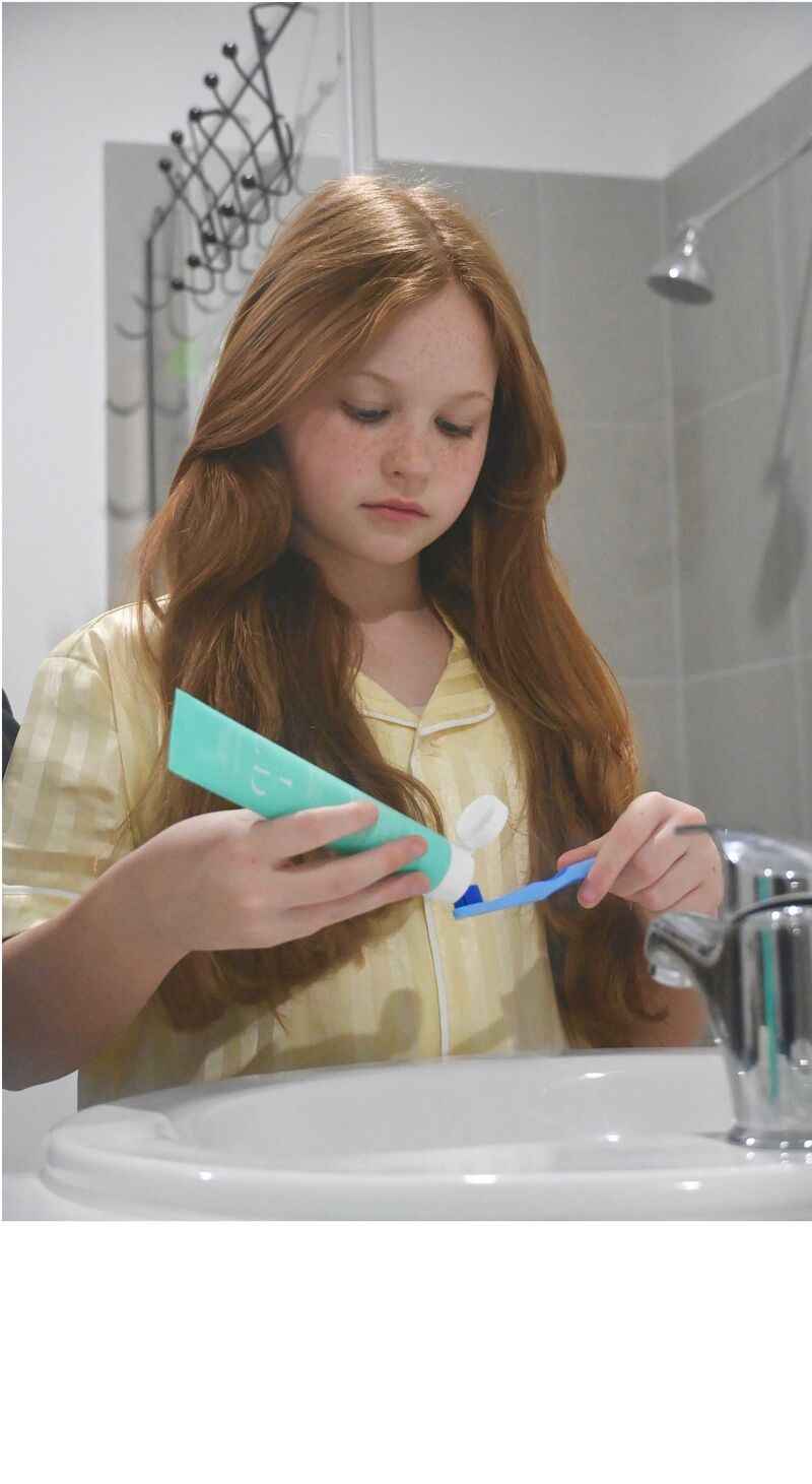 Girl squeezing Flossy & Pure nano-hydroxyapatite toothpaste onto her toothbrush at the bathroom sink