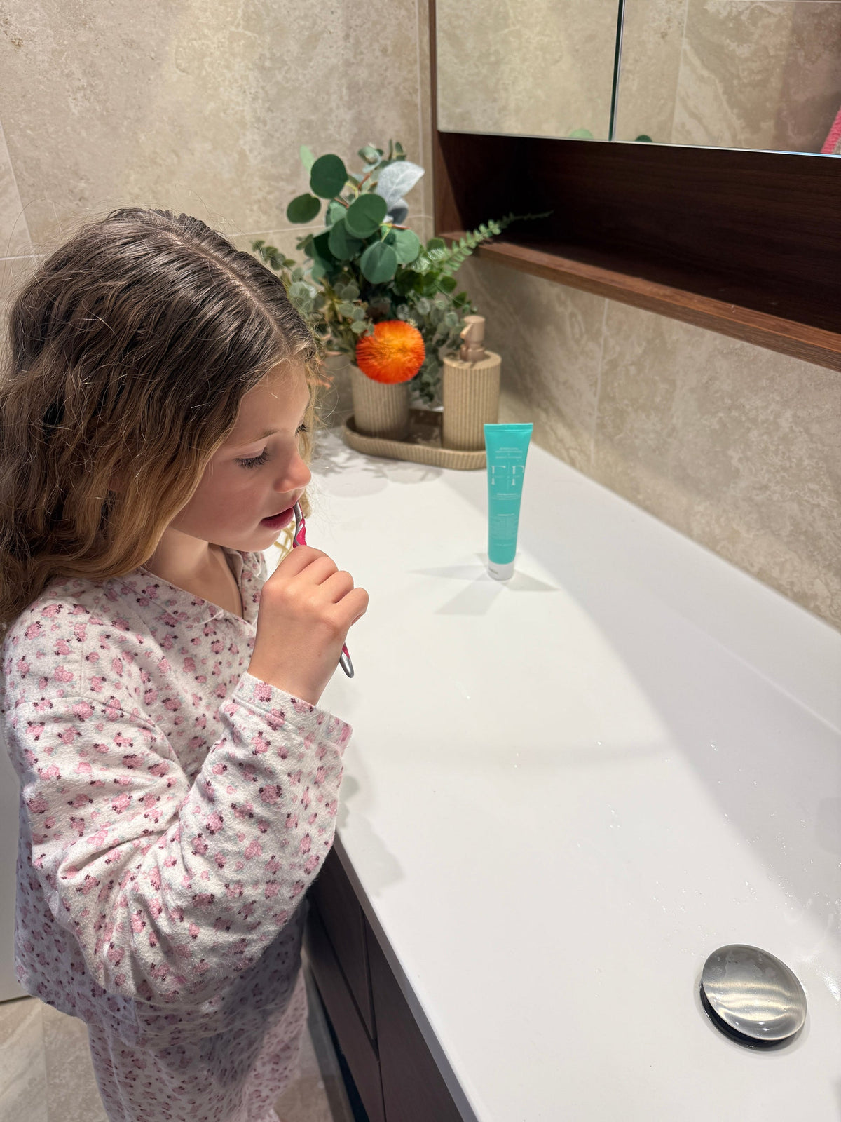 Girl brushing her teeth at the bathroom vanity with Flossy & Pure family toothpaste on the bench