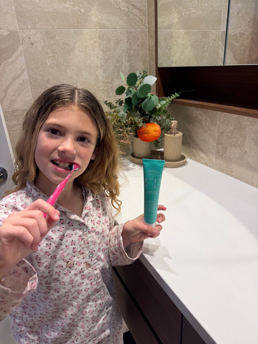 Girl brushing her teeth while holding Flossy & Pure nano-hydroxyapatite toothpaste in her bathroom