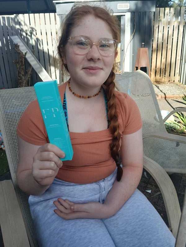 Teenage girl with a long red plait in the backyard, holding up a Flossy and Pure toothpaste box