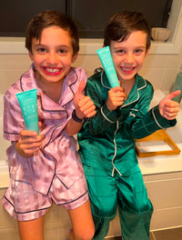 Two kids in pyjamas giving a thumbs up with their Flossy & Pure fluoride-free family toothpaste